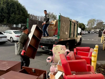 Junk removal crew loading red upholstered furniture and wooden items onto hauling truck