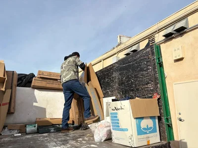 Worker removing cardboard boxes and metal debris from commercial rooftop