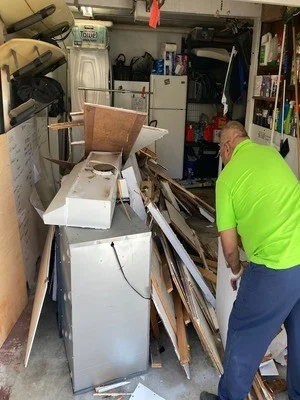 Garage junk removal showing white appliance, wooden furniture, and mixed debris being loaded for hauling