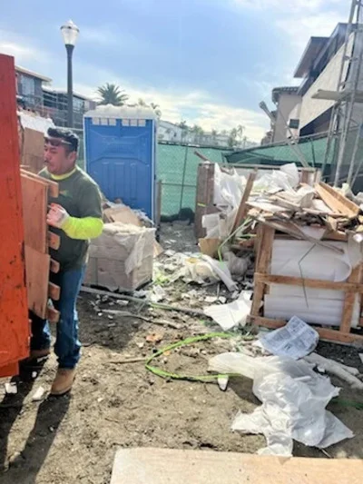 Worker in safety gear removing mixed commercial debris and wood waste from industrial lot