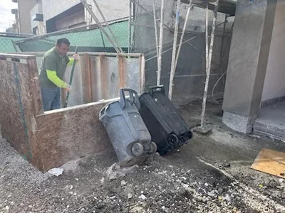 Worker in safety vest removing metal drums and industrial equipment from commercial site