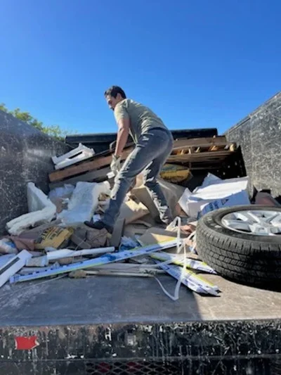 Worker loading mixed debris including wood, metal, and tires into hauling truck