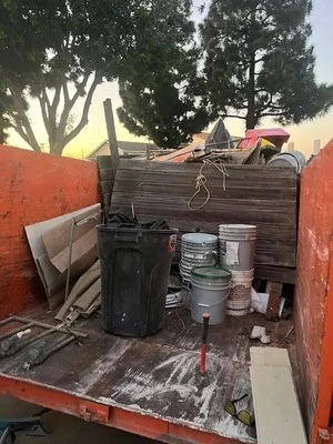 Truck bed filled with wooden furniture, paint cans, and mixed household junk ready for disposal