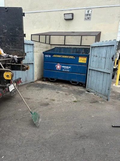 Large blue commercial waste bin removal from industrial facility with metal gates