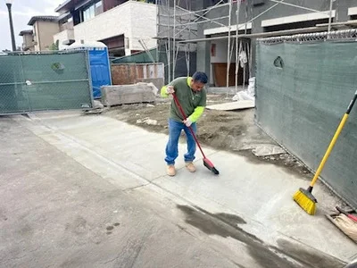 Worker sweeping concrete debris from construction site with green containment barriers