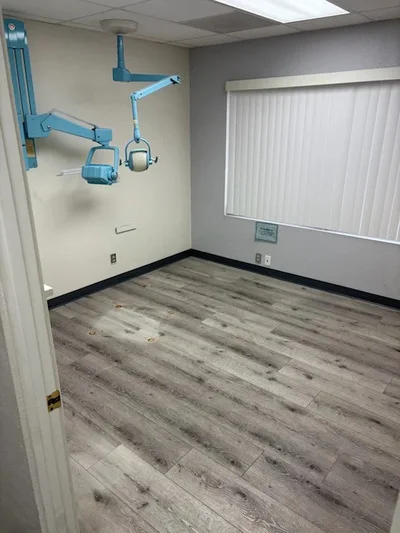 Empty medical office room with removed surgical lights and cleared walls, vinyl plank flooring visible