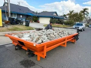 Orange trailer loaded with concrete rubble and construction debris in driveway