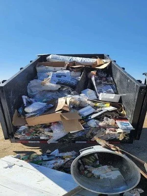 Truck bed filled with mixed junk, boxes, clothing, and household waste ready for hauling