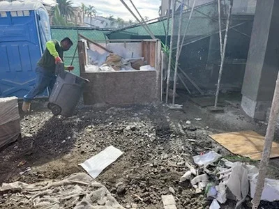 Worker removing concrete rubble and construction debris from residential site with blue dumpster