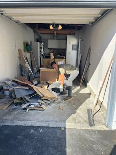 Before photo of cluttered garage with wood scraps, cardboard boxes, and mixed debris ready for removal