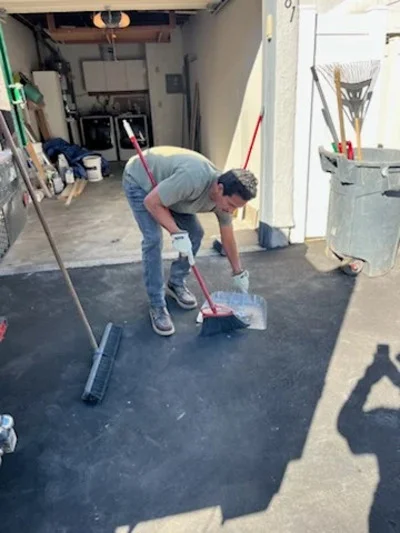 Worker removing debris and junk from garage floor with shovel and broom