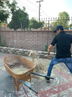 Worker demolishing brick wall with wheelbarrow of concrete and brick debris