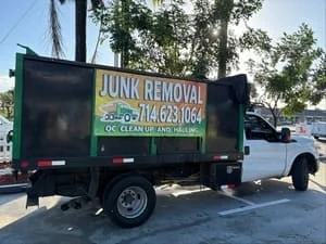 Green and black junk removal truck with open bed, parked on residential street