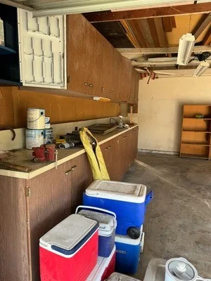 Empty garage with removed wooden cabinets, coolers, and debris cleared from floor